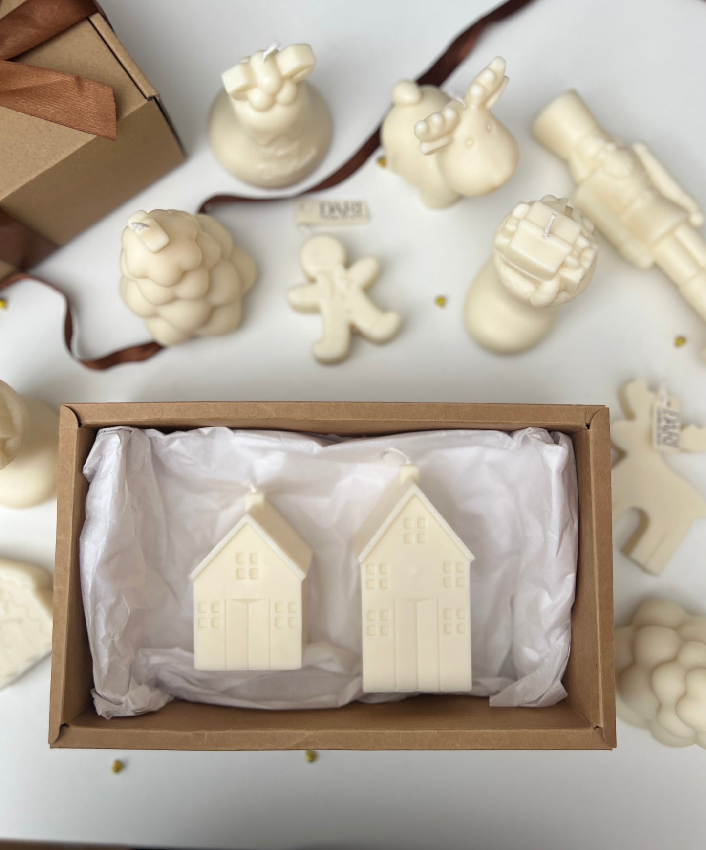 Two white candle  houses in a box with other candles  figures on a light background