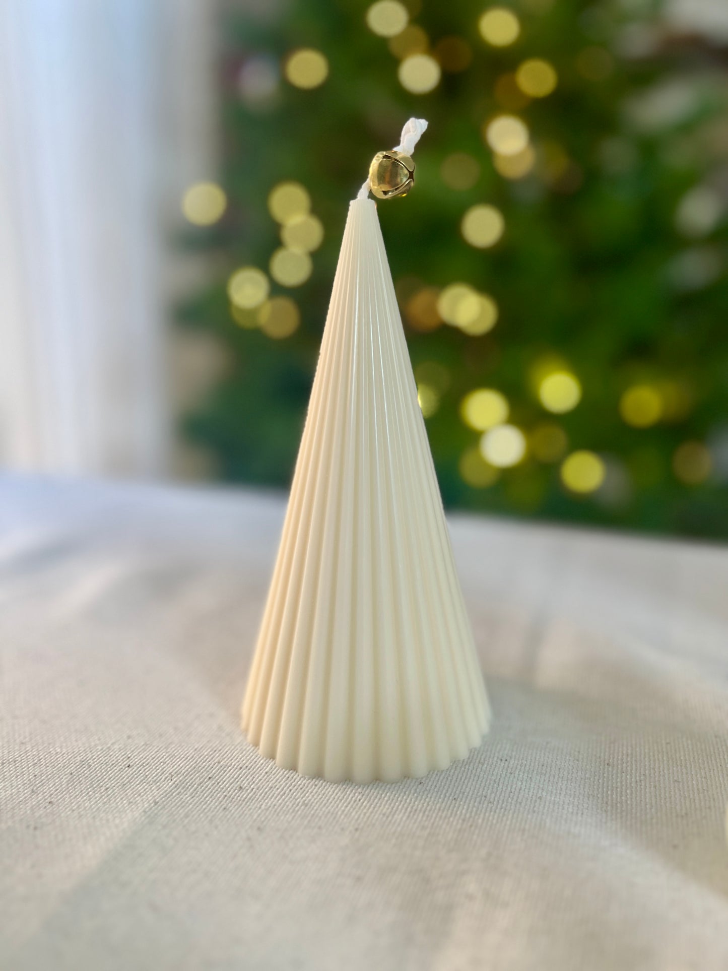 White textured cone-shaped christmas tree  candle on a light surface with a blurred green and gold background