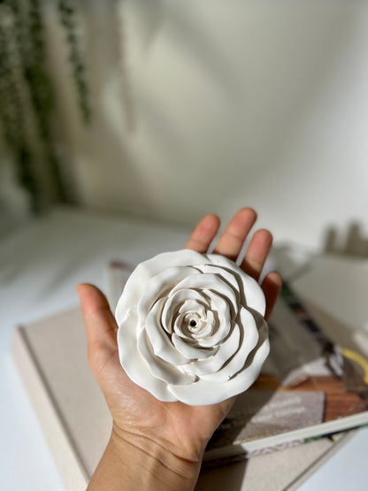 Hand holding a white ceramic flower against a blurred background