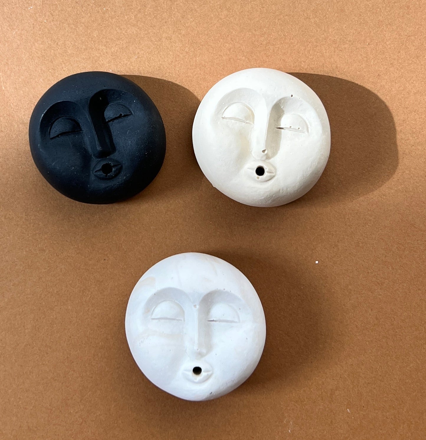 Three white and black moon face incense holderson a brown surface
