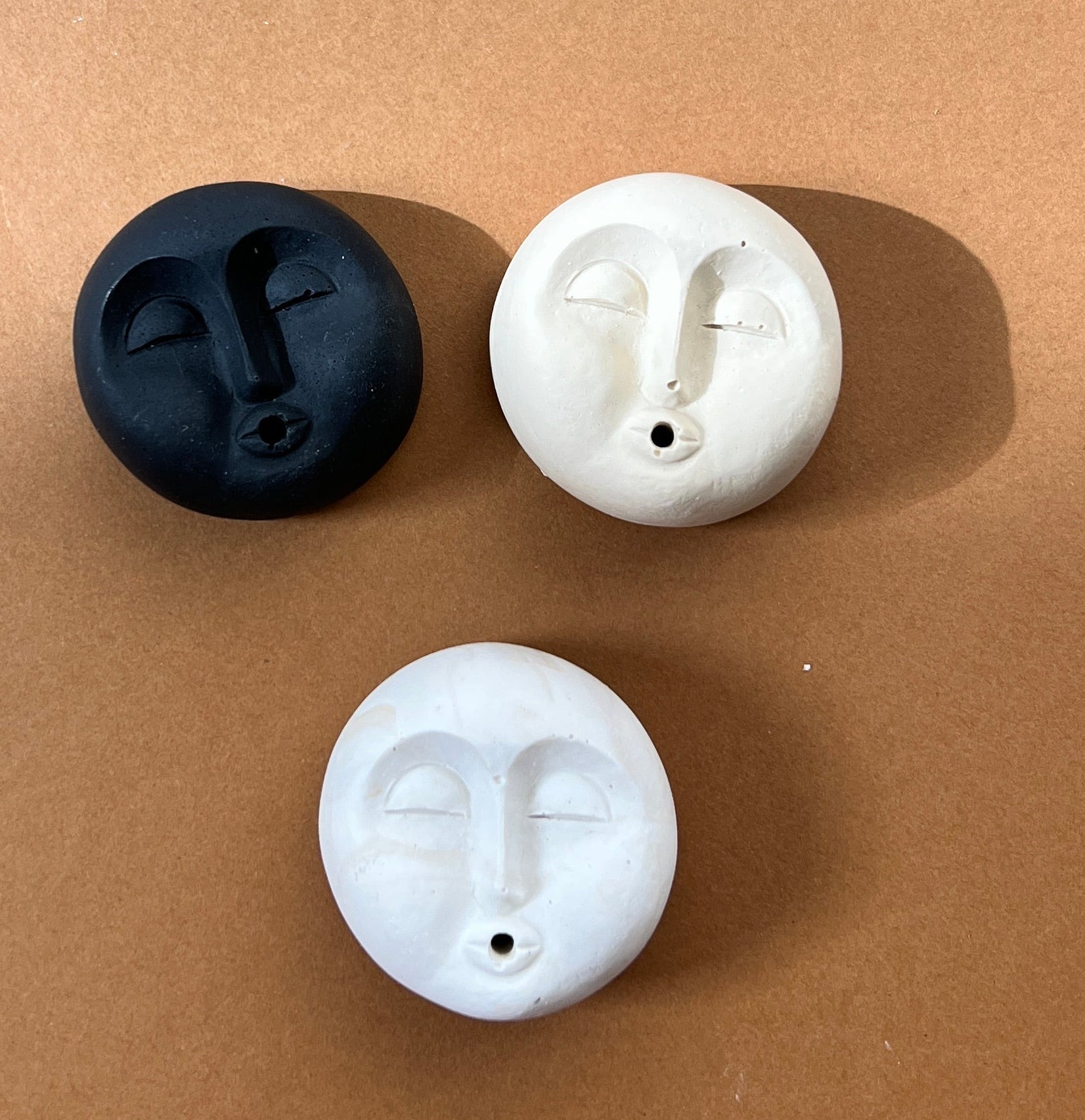 Three white and black moon face incense holderson a brown surface