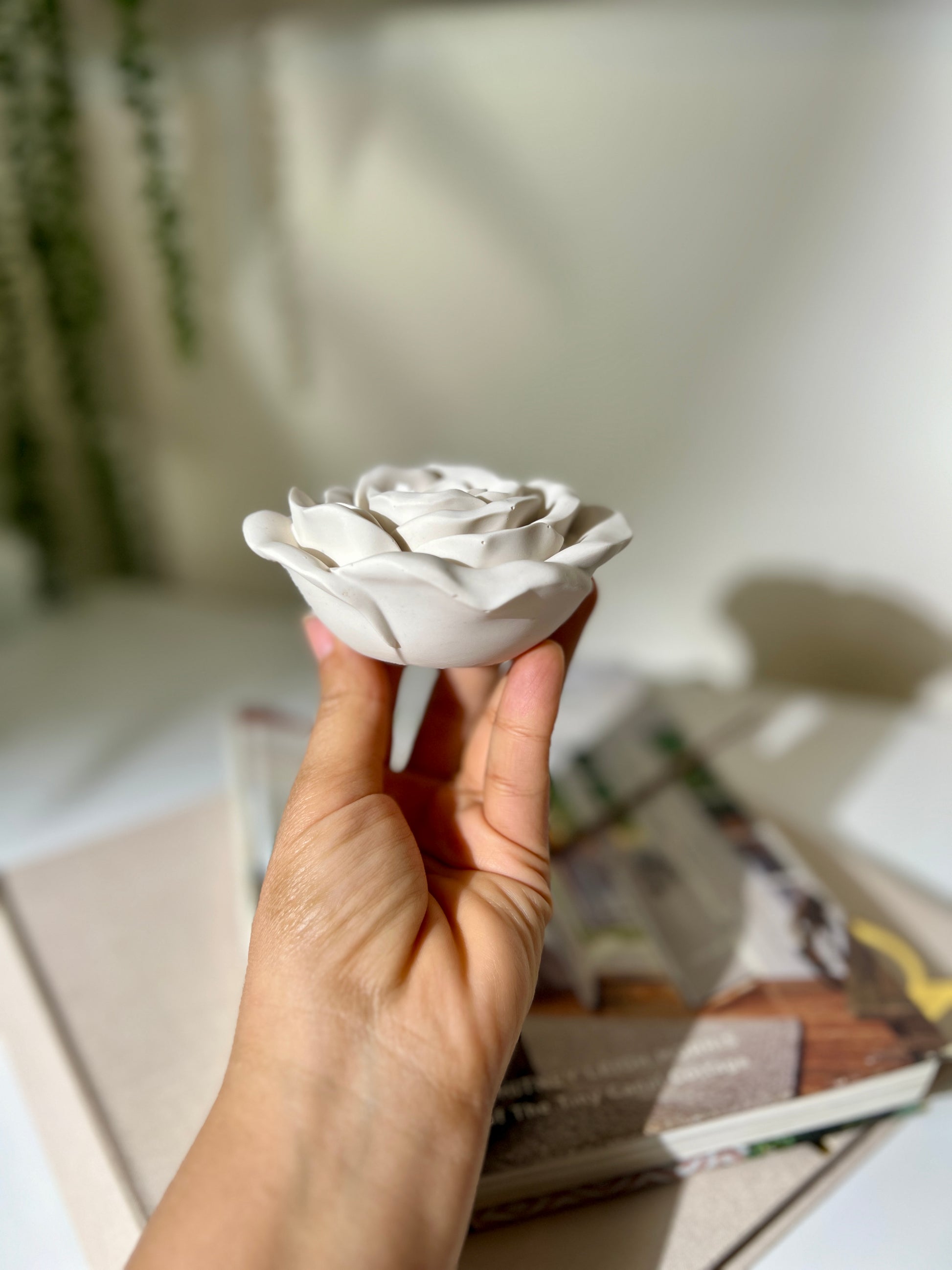 Hand holding a white ceramic rose against a blurred indoor background